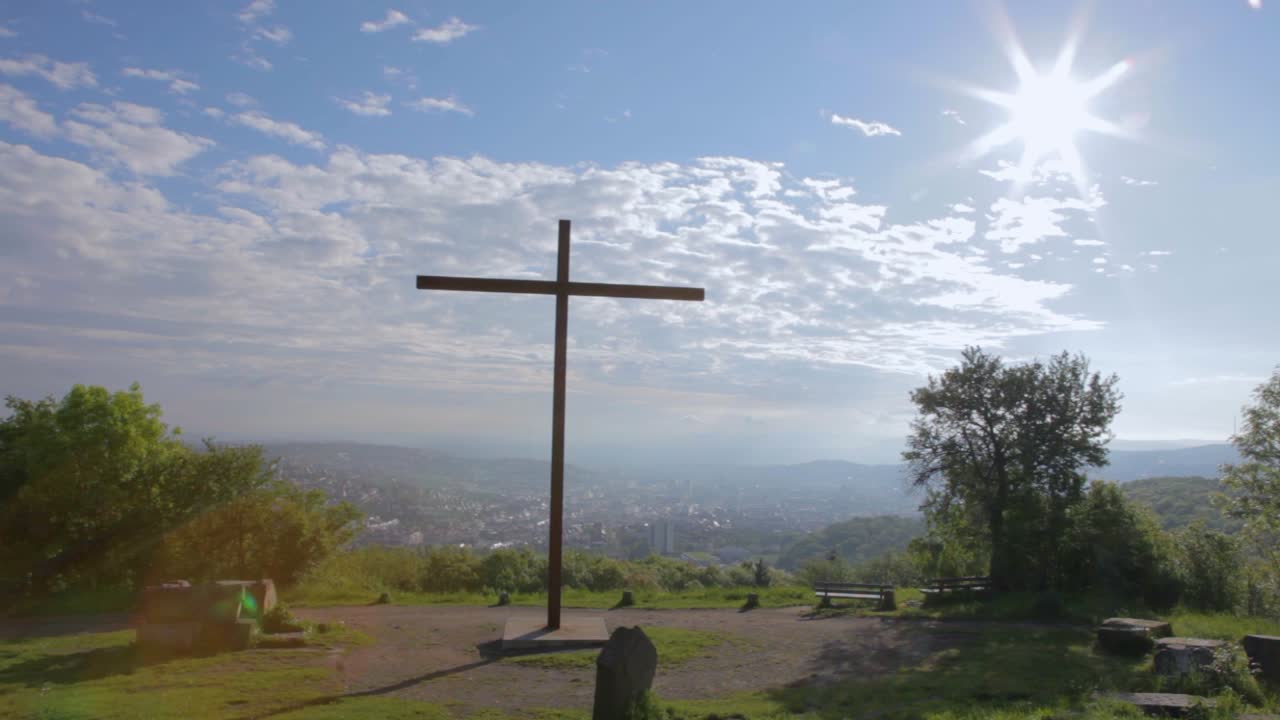 큰 나무 십자가가 밝고 은 하늘 아래 도시를 내려다보는 언덕 위에 서 있습니다.