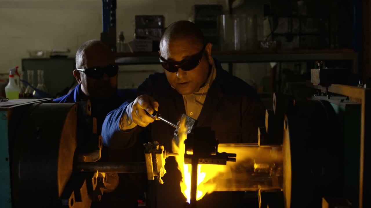 Deux ouvriers masculins matures soufflant le verre dans une verrerie 4k