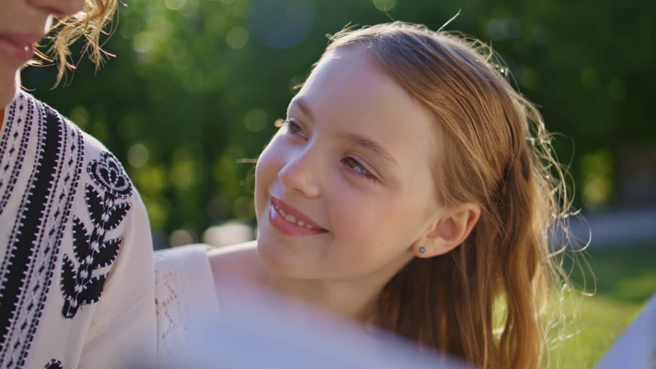 Small kid watching book parent at park lawn closeup. Daughter mother resting