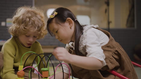 little girl and little boy playing with wooden pieces that move in a wire in classroom in a montessori school