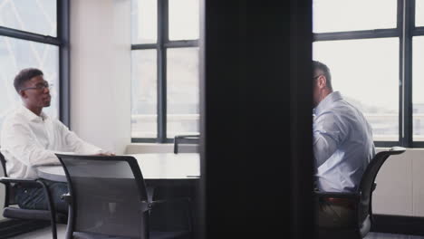 a black and a white businessman talking in a meeting room, arc shot, seen through glass wall