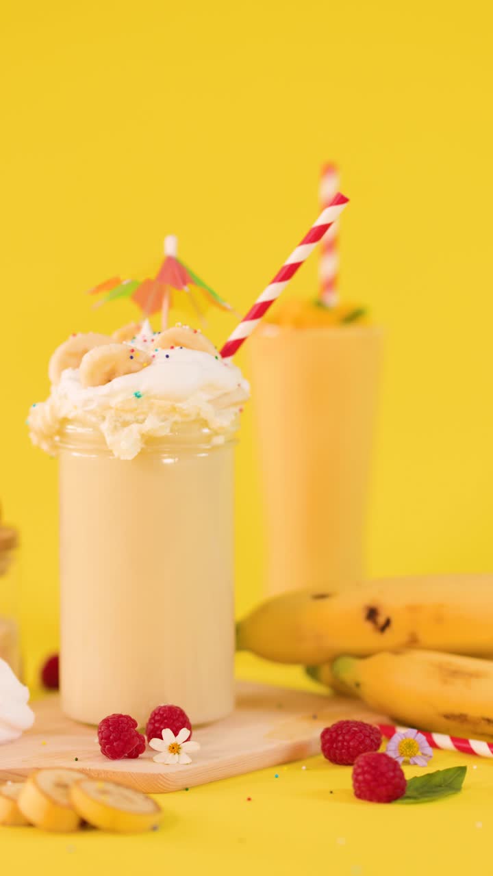 Frullato cremoso alla banana con panna montata, guarnizione di frutta e biscotti su sfondo giallo vivace da studio