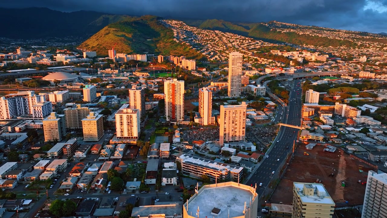 Paesaggio variegato di Honolulu nella luce arancione del sole al tramonto. Drammatiche nuvole scure si muovono sulla città sopra le montagne. Vista aerea