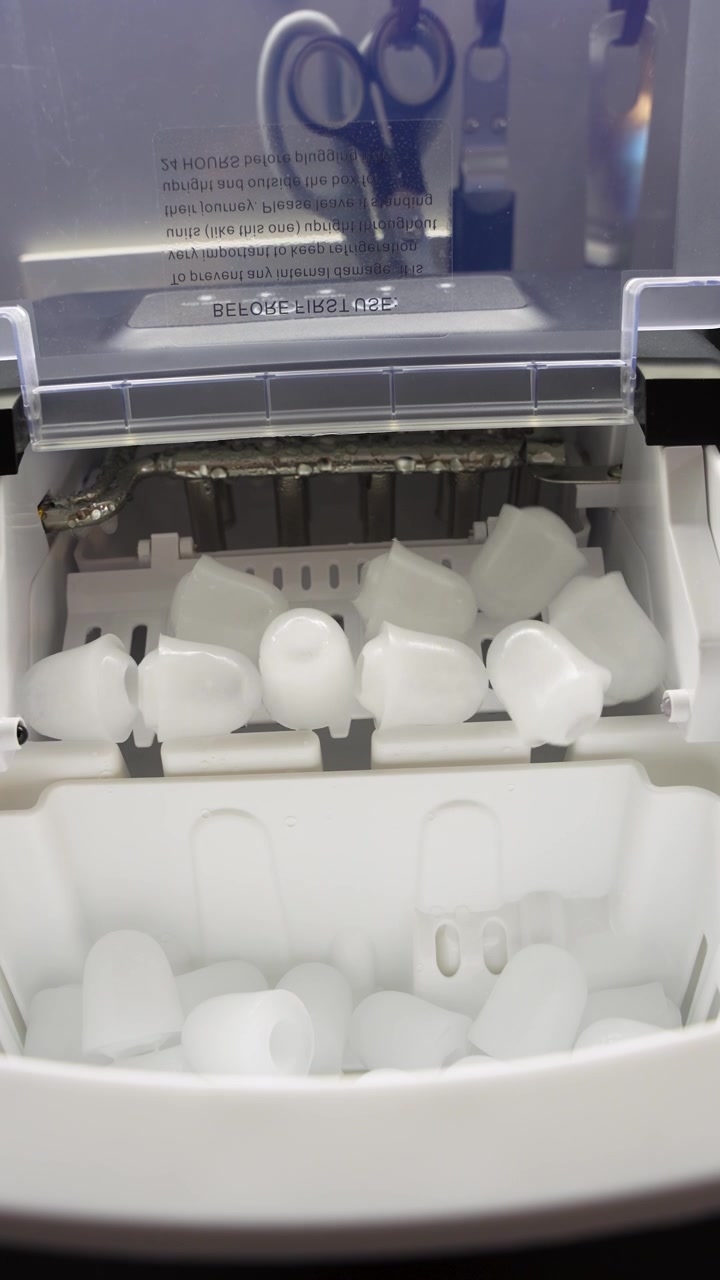 Primo piano verticale di un fabbricatore di ghiaccio portatile che eroga ghiaccio a proiettile fresco nel cestello, mostrando la produzione automatica di ghiaccio all'interno di un elettrodomestico compatto da banco.