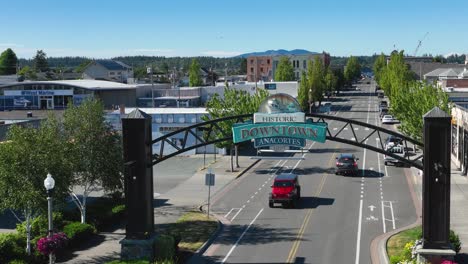 Aerial-shot-of-cars-passing-underneath-the-Anacortes,-WA-welcome-sign-on-main-street