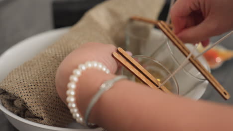 close-up hand view of lady arranging glass cups inside white bowl using sack bag for securing, preparing candle holders with wicks inside cups for crafting or decorative purposes