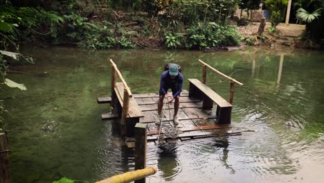 a man is pulling on a rope to cross a river on a wooden raft in a lush colombian forest setting