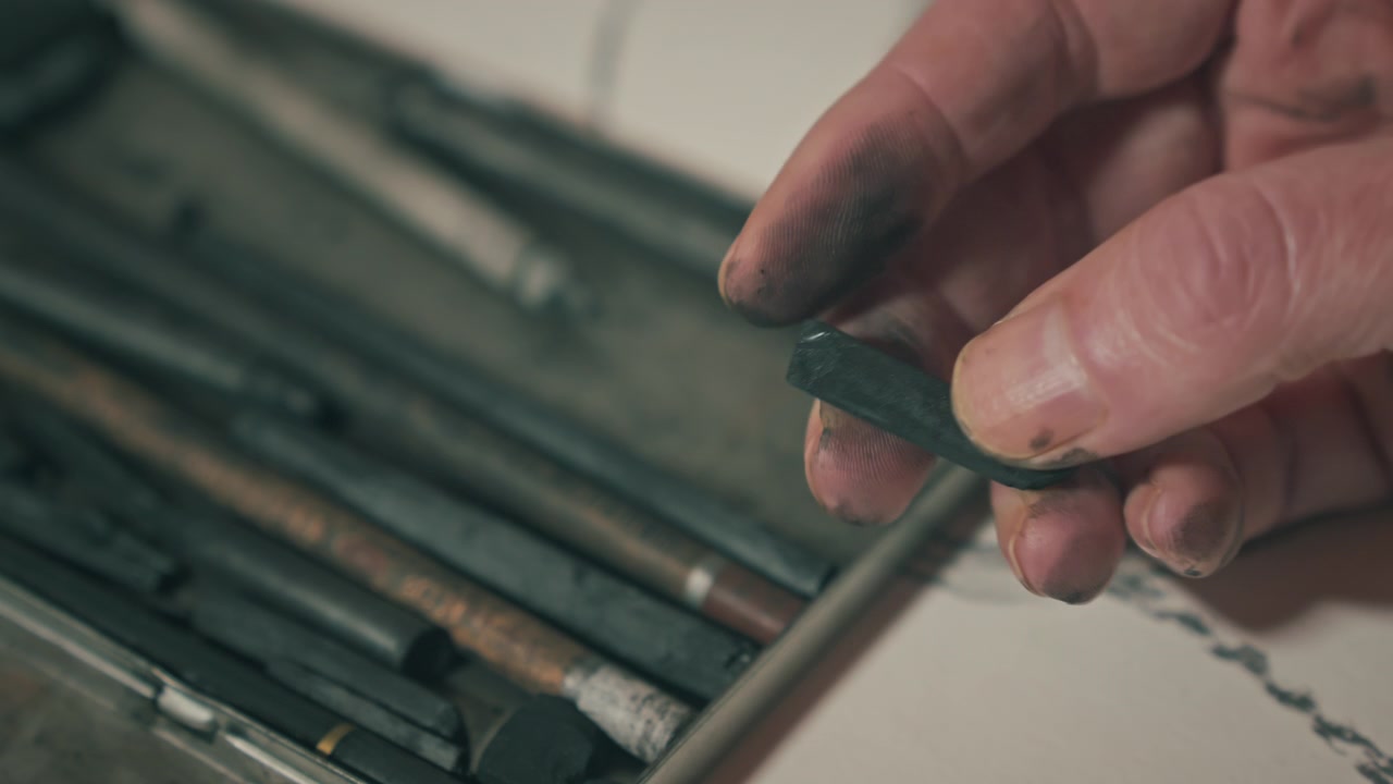 Close-up of dirty, smudged hands rolling charcoal, highlighting raw creativity, tactile engagement, and immersive artistic workflow.