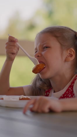 grimacing little girl bites too hot curd fritter with sour cream sitting at table in street cafe closeup slow motion. shock of hot food