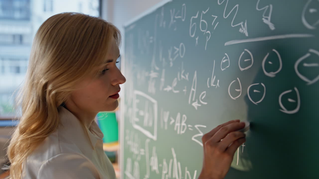 School teacher solving math equations on blackboard with chalk closeup