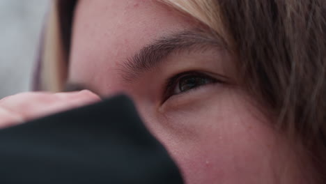 close-up face view of young woman rubbing her nose in cold weather, red, flushed skin highlights winter chill, blurred background of snowy trees