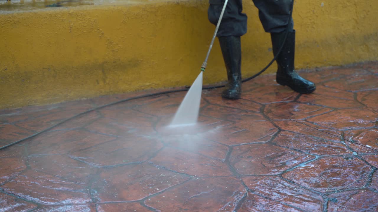 Closeup on waist down shot of person power washing the pavement toward the camera in a park