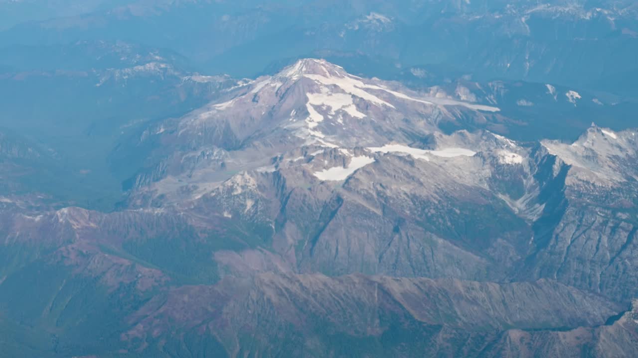 Snow-capped mountain peak viewed from a drone at high altitude, with dramatic shadows and ridges surrounded by deep valleys