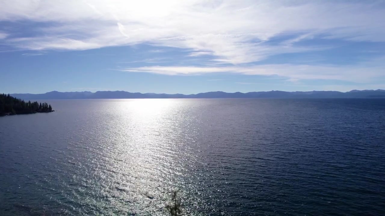 Filmische Luftaufnahme von schimmerndem Wasser mit heller Sonnenreflexion, die eine friedliche und weite Szene schafft
