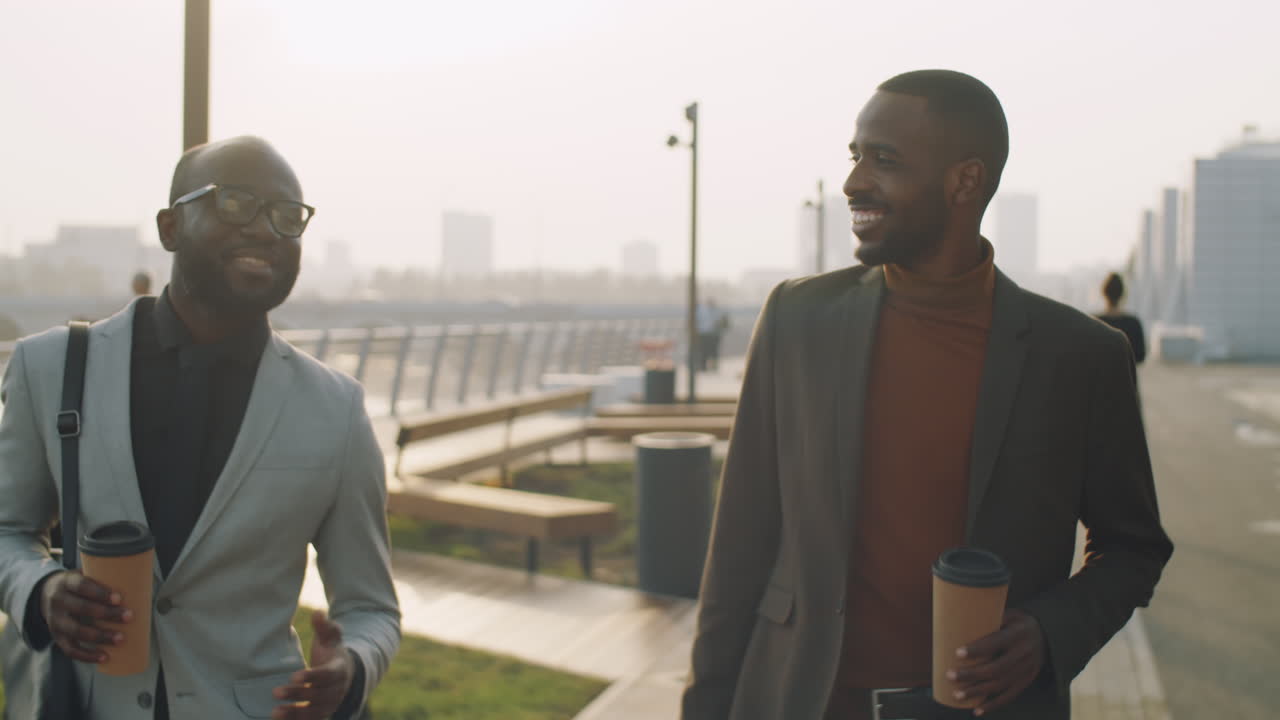 hombres de negocios afroamericanos caminando con café al aire libre y hablando