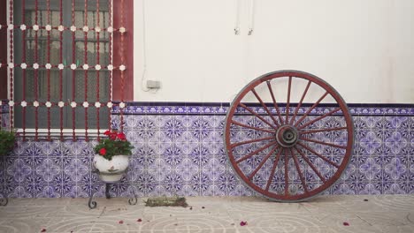 typical spanish yard with an old wheel, a few plants with red flowers and blue tiles