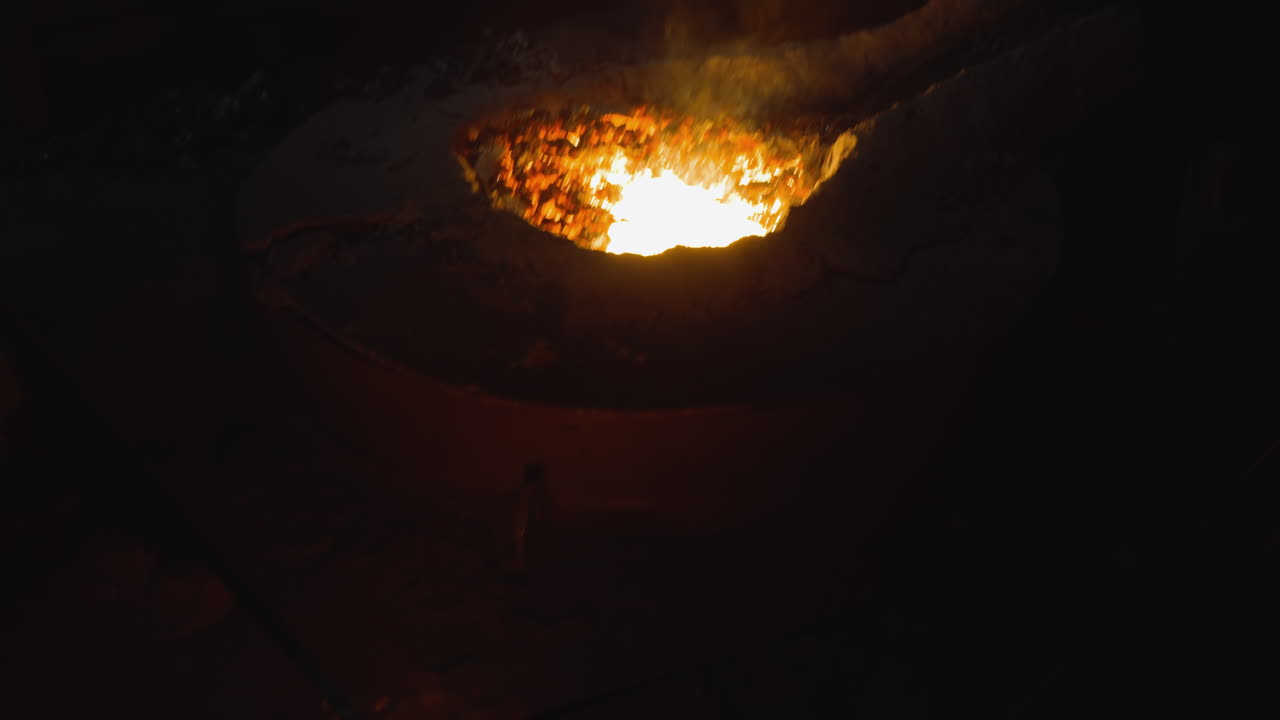 Pouring molten steel into a mold at a darkened steel foundry, fiery glow