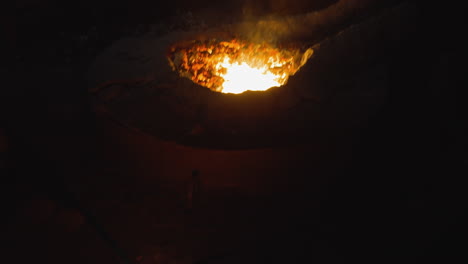 pouring molten steel into a mold at a darkened steel foundry, fiery glow