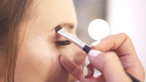 vista de cerca y artista de maquillaje cepillando las cejas de una modelo de moda mientras la prepara para una sesión de fotos. disparo en cámara lenta