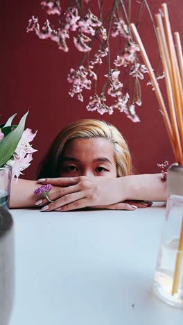 woman hiding face behind hands in front of flowers