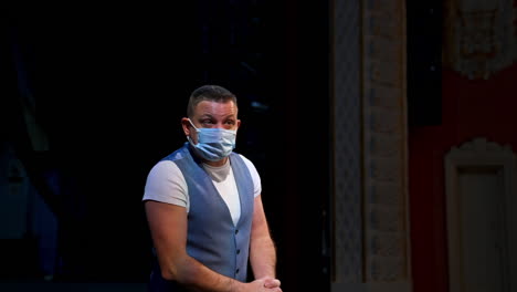 man in medical mask on scene. actor in protective mask is talking and gesticulating a lot while standing on stage in the theater. pandemic in the world.