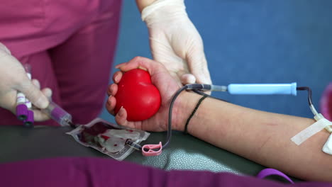 unrecognized woman's hand holding a red heart. nurse touches the iv drip filling with donor's blood. close up.