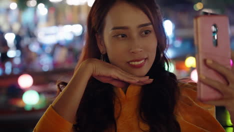 Close-up-of-attractive-Vietnamese-woman-in-traditional-dress-taking-phone-selfie-next-to-river-at-night