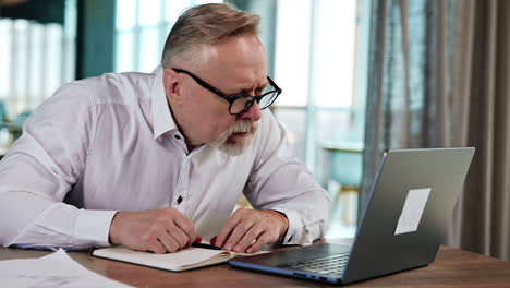 positive smiling g businessman in white shirt and glasses leans closer to his laptop. puzzled man looks at computer screen.
