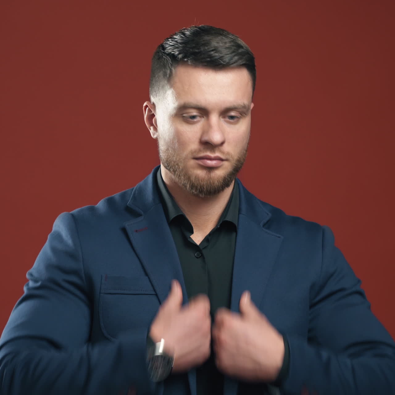 Cheerful young man in suit standing and touching his jacket. Handsome businessman. Dark red backgound. Half waist selective focus.