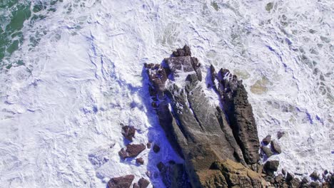 Vista-Aérea-De-Arriba-Hacia-Abajo-De-Las-Olas-Rompiendo-En-Una-Roca-En-Las-Costas-De-Cantabria,-España-Durante-Un-Día-Soleado-En-Cámara-Lenta