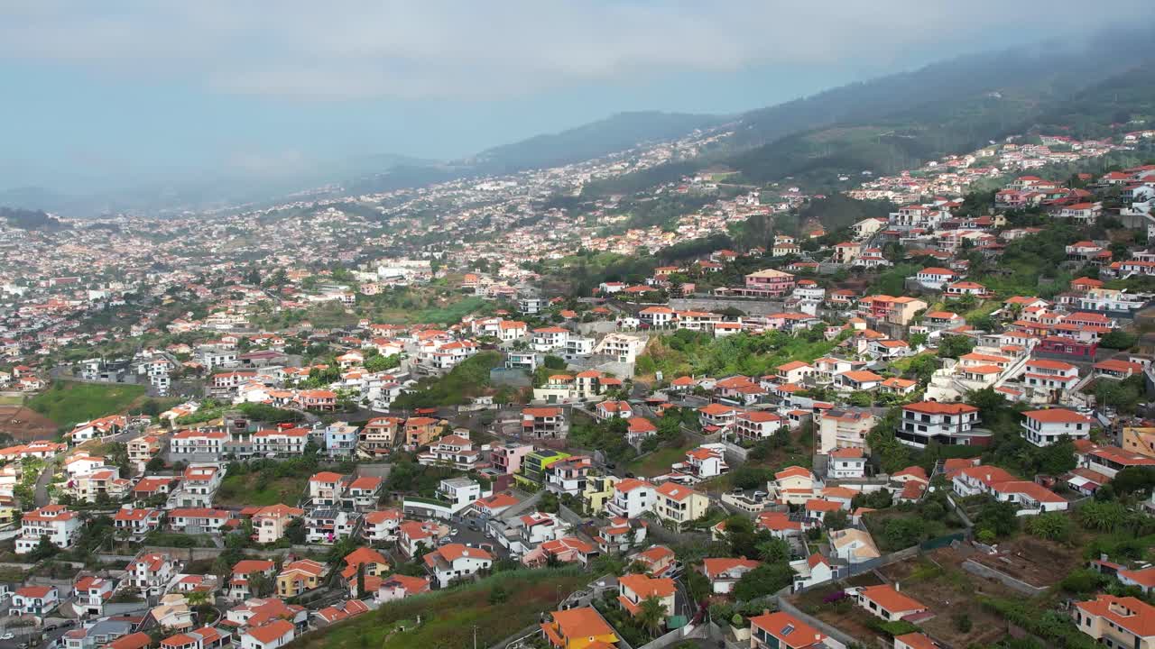 Filmato aereo con drone di un pendio costiero con vista sull'oceano e ville bianche circondate dal verde. Funchal, Madeira, Portogallo
