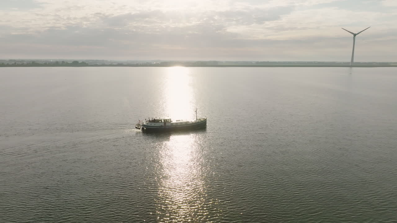 Aerial dolly in shot of the Dutch boat Luxe Motor crossing the calm sea with a wind turbines in the background. in Holland