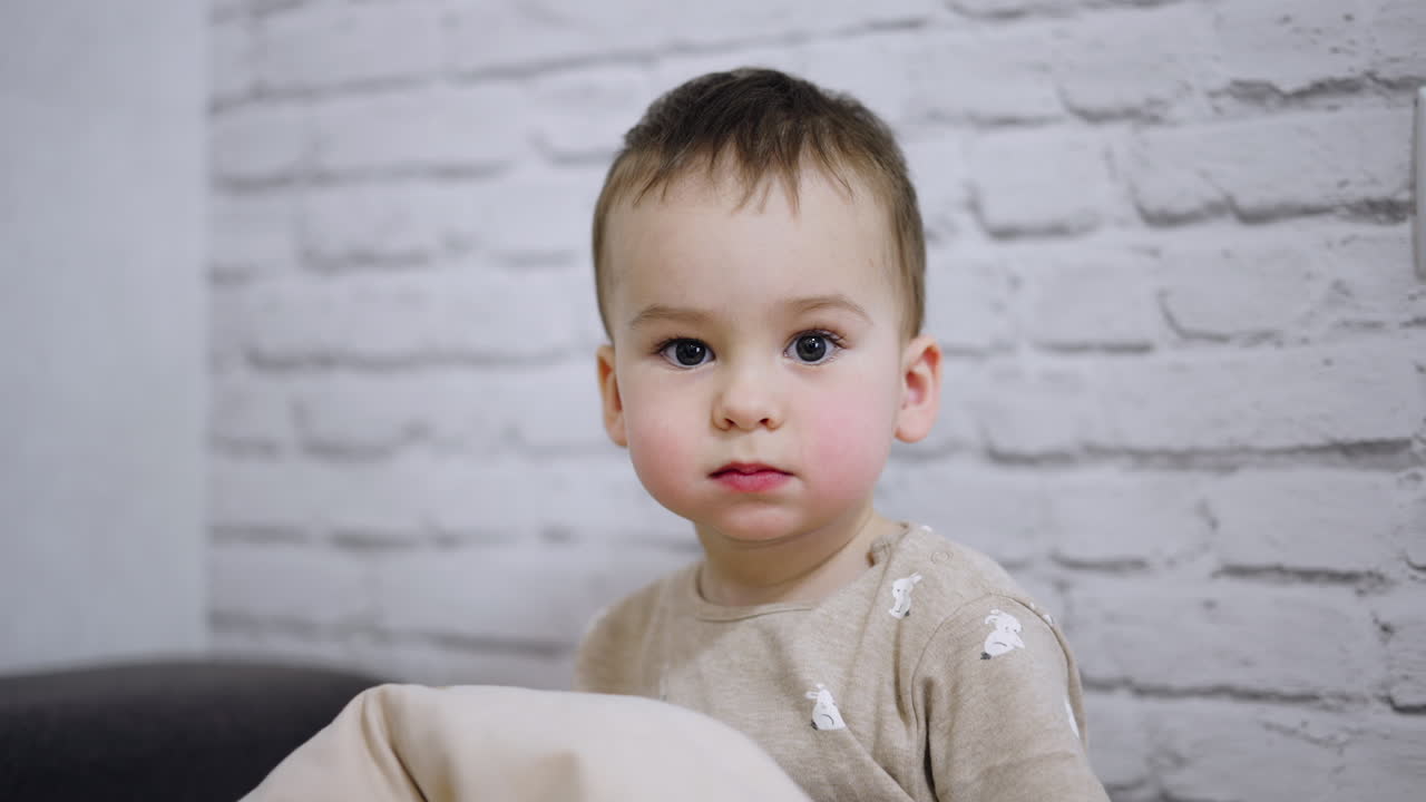 Beautiful Caucasian baby with adorable rosy cheeks. Serious toddler smiles sweetly to camera. White backdrop.