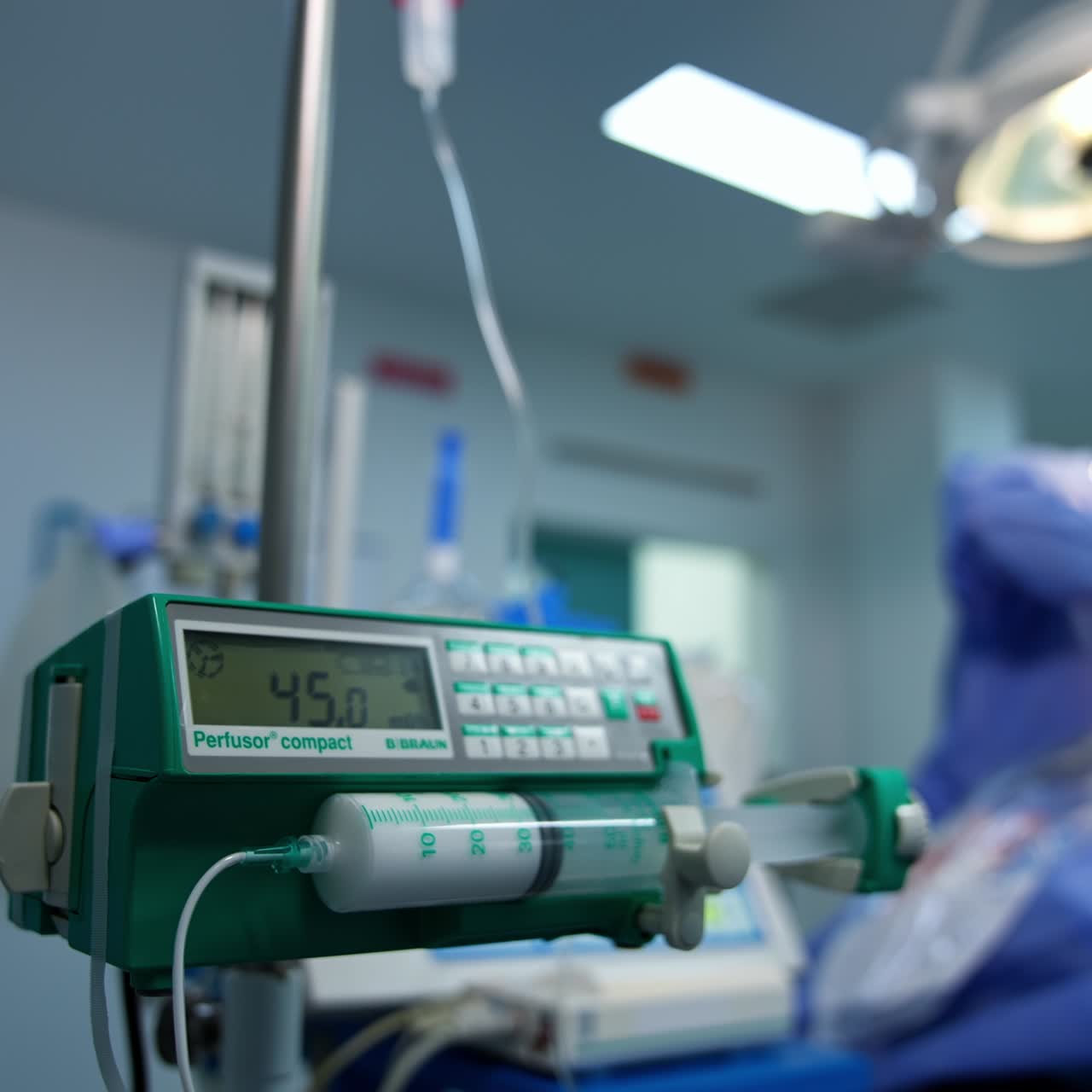 Attrezzatura in una moderna sala operatoria. Apparecchio contenente una siringa con medicinale bianco per il dosaggio graduale. Primo piano. Intervento chirurgico sullo sfondo