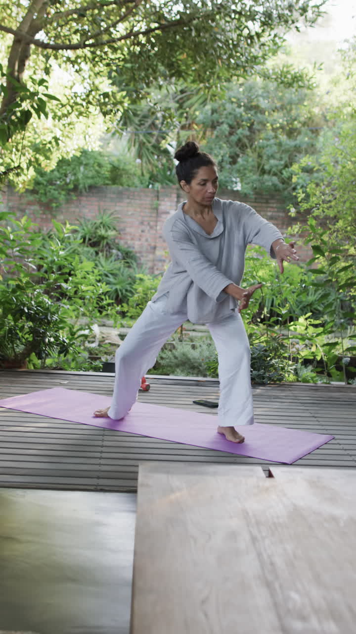 Vertical video of focused biracial woman practicing yoga on sunny terrace, slow motion