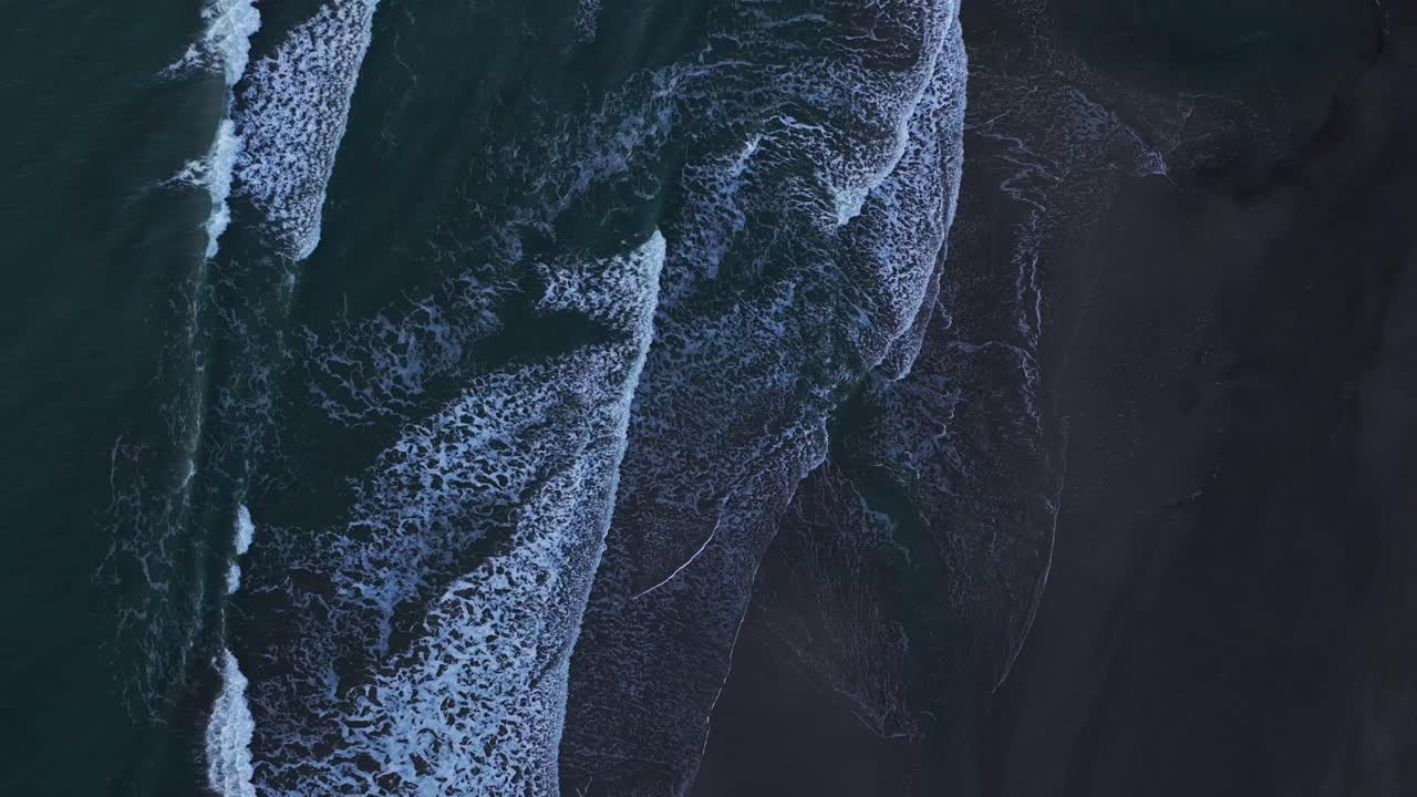 Stationary drone shot looking down at white waves hitting the beach at sunset