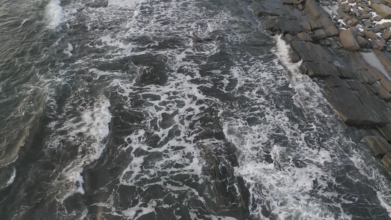 Seguendo le onde che si infrangono su una costa rocciosa durante l'alba invernale. AEREO.