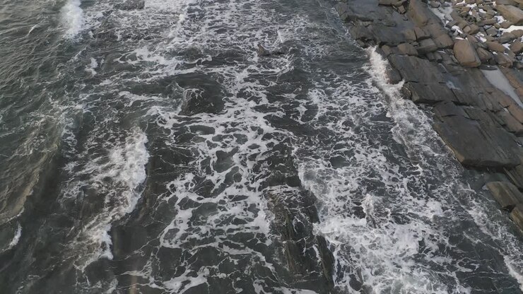 Seguendo le onde che si infrangono su una costa rocciosa durante l'alba invernale. AEREO.