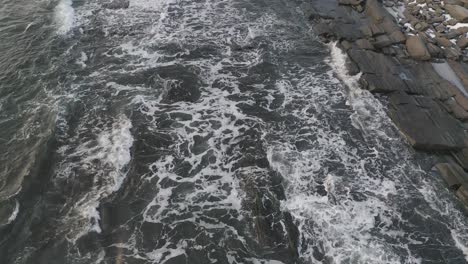 following waves in as they wash over a rocky shoreline during winter sunrise aerial