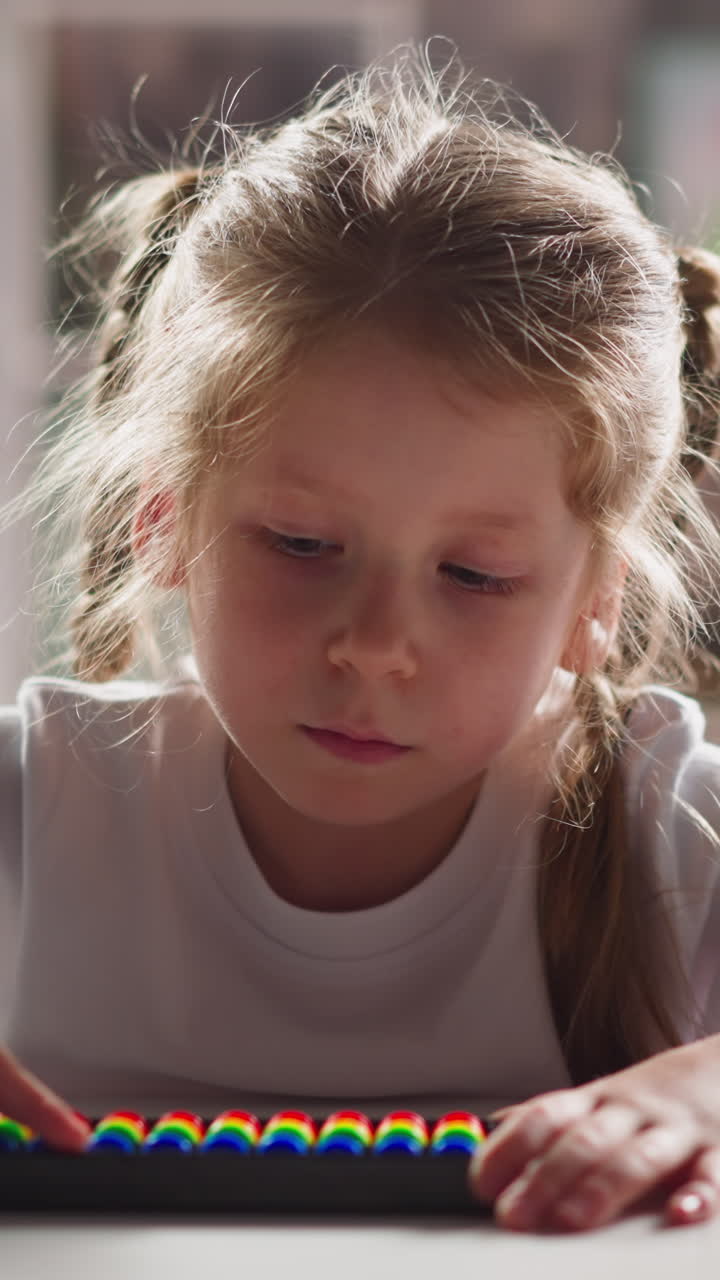 Thoughtful little kid with blonde plaits touches colorful abacus beads by finger during mental arithmetic lesson close view slow motion