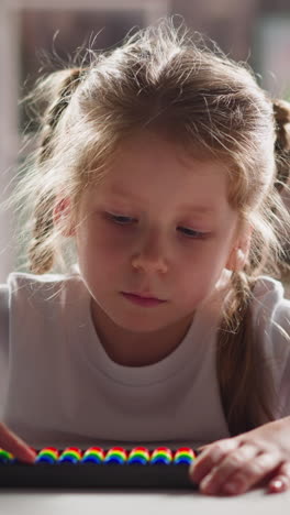 thoughtful little kid with blonde plaits touches colorful abacus beads by finger during mental arithmetic lesson close view slow motion
