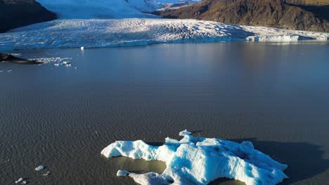 Calved-Iceberg-in-Sunny-Glacier-Lake,-Cinematic-Aerial-Reveal