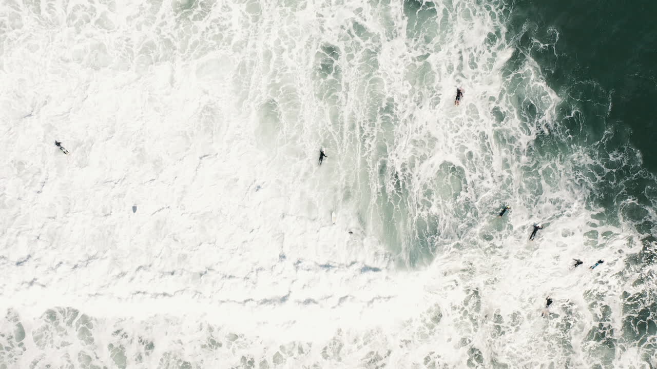 Top-down aerial drone shot of people surfing and trying to catch waves in white water