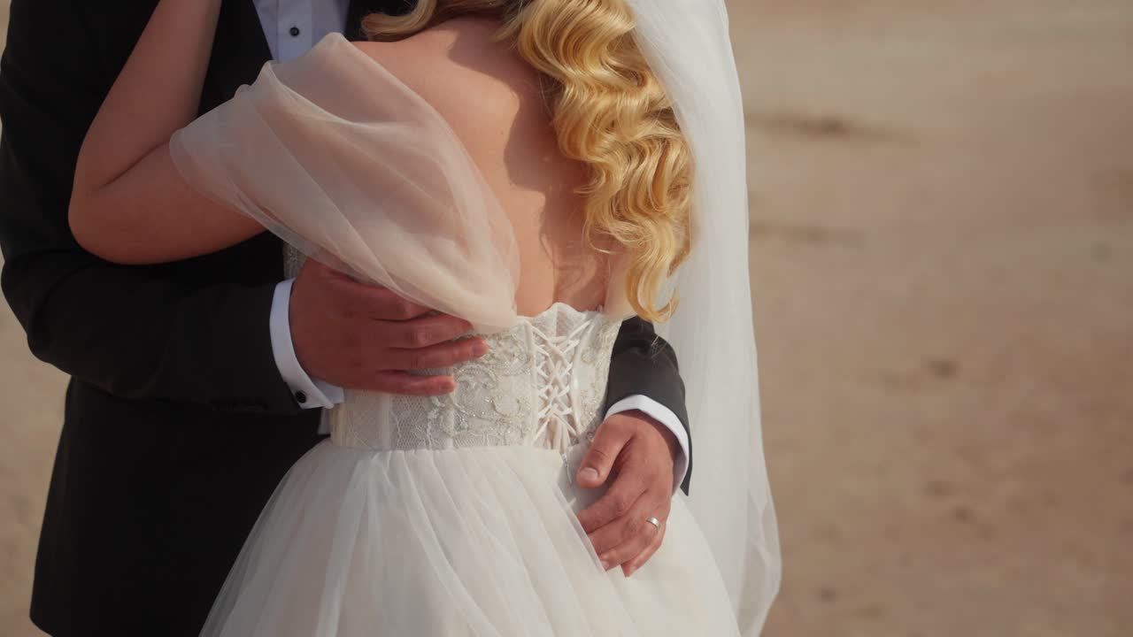 Nærbillede af et brudepar, der omfavner hinanden under et romantisk strandbryllup, fremhæver den elegante kjole og det ømme øjeblik af kærlighed og forbindelse