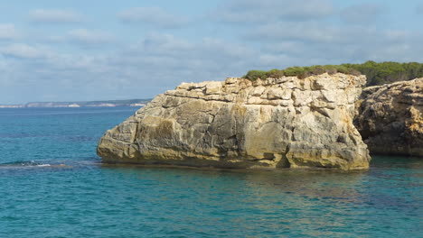 big rock illuminated by the morning light in the azure sea on the south cost of menorca island