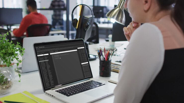 Donna caucasica seduta alla scrivania che osserva la codifica e l'elaborazione dei dati sullo schermo del laptop.