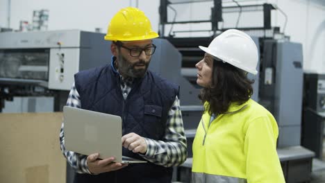 confident technicians discussing work while standing with laptop