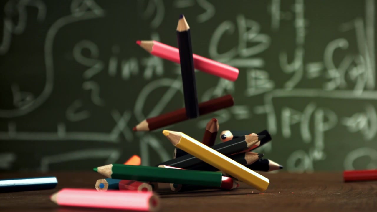 Colorful Pencils Falling onto a Desk in Front of a Math Chalkboard