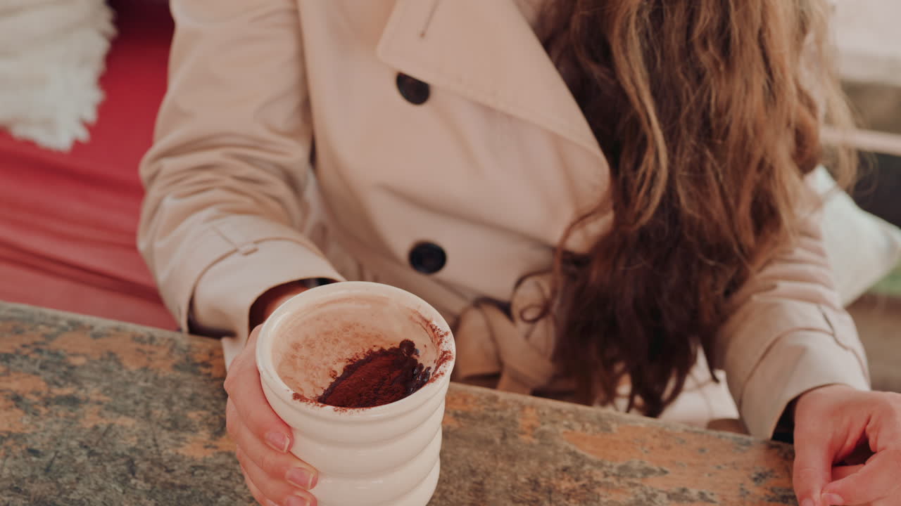 Woman's hand holding a cup of hot chocolate, with cocoa powder visible on top