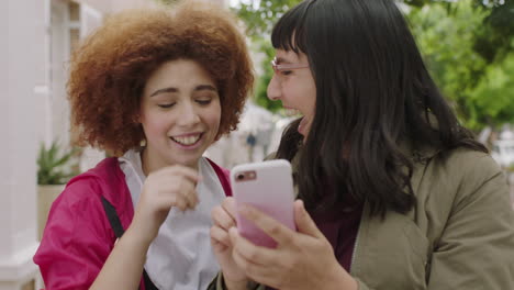 portrait of two young women friends posing taking selfie using smartphone smiling cheerful enjoying browsing photos in urban background